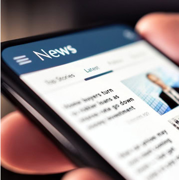 Close-up of a hand holding a smartphone displaying a news website.