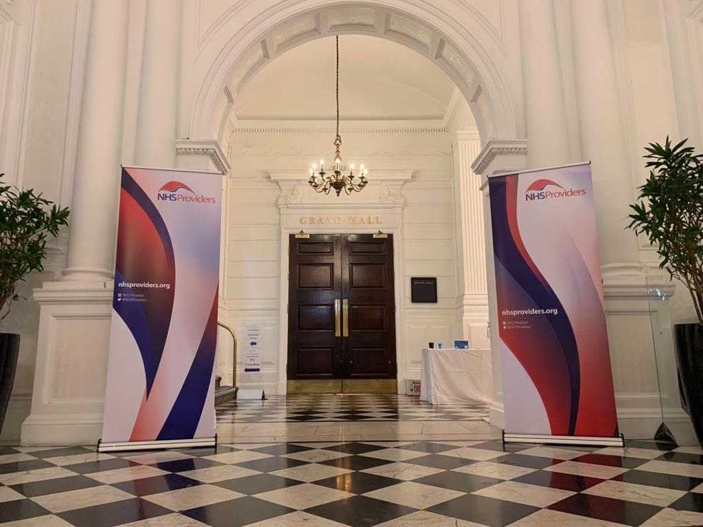 Entrance to a grand hall with checkered floor, chandeliers, and two NHS Providers banners on either side.